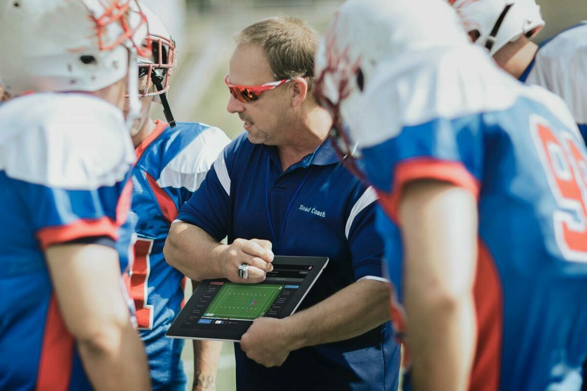 Ein American-Football-Trainer wendet sich während einer Auszeit an seine Mannschaft und nutzt dabei die Echtzeit-Leistungsdaten, die von den Tracking-Geräten der Spieler geliefert werden.