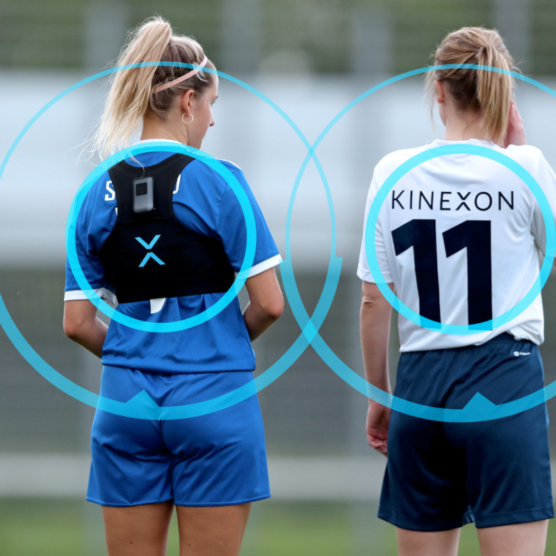 Two women athletes equipped with mobile player tracking devices discuss strategies during a timeout at a training session.