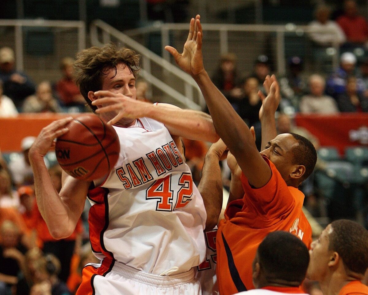 A basketball player comes down with a rebound at the end of a game while surrounded by defenders.