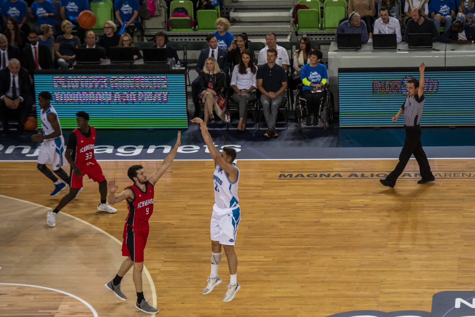 Ein Basketballspieler in der Mitte des Sprungs, mit ausgestrecktem Arm, der den Ball für einen 3-Punkte-Wurf in Richtung des Reifens freigibt.