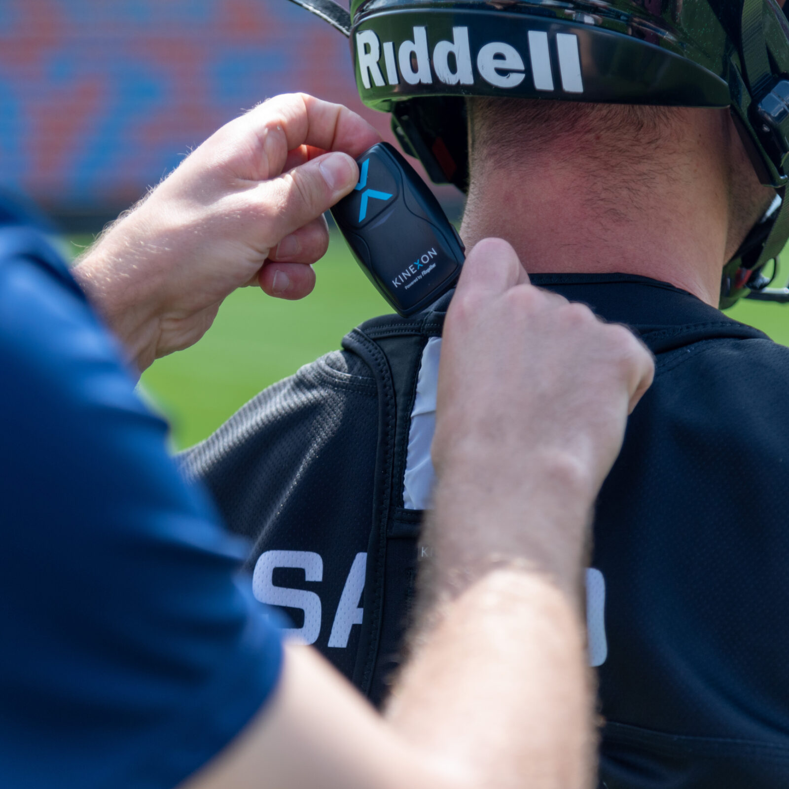 A tackle football player gets his gps athlete tracker from his coach, which slips into a lightweight vest and is not noticeable to the player.