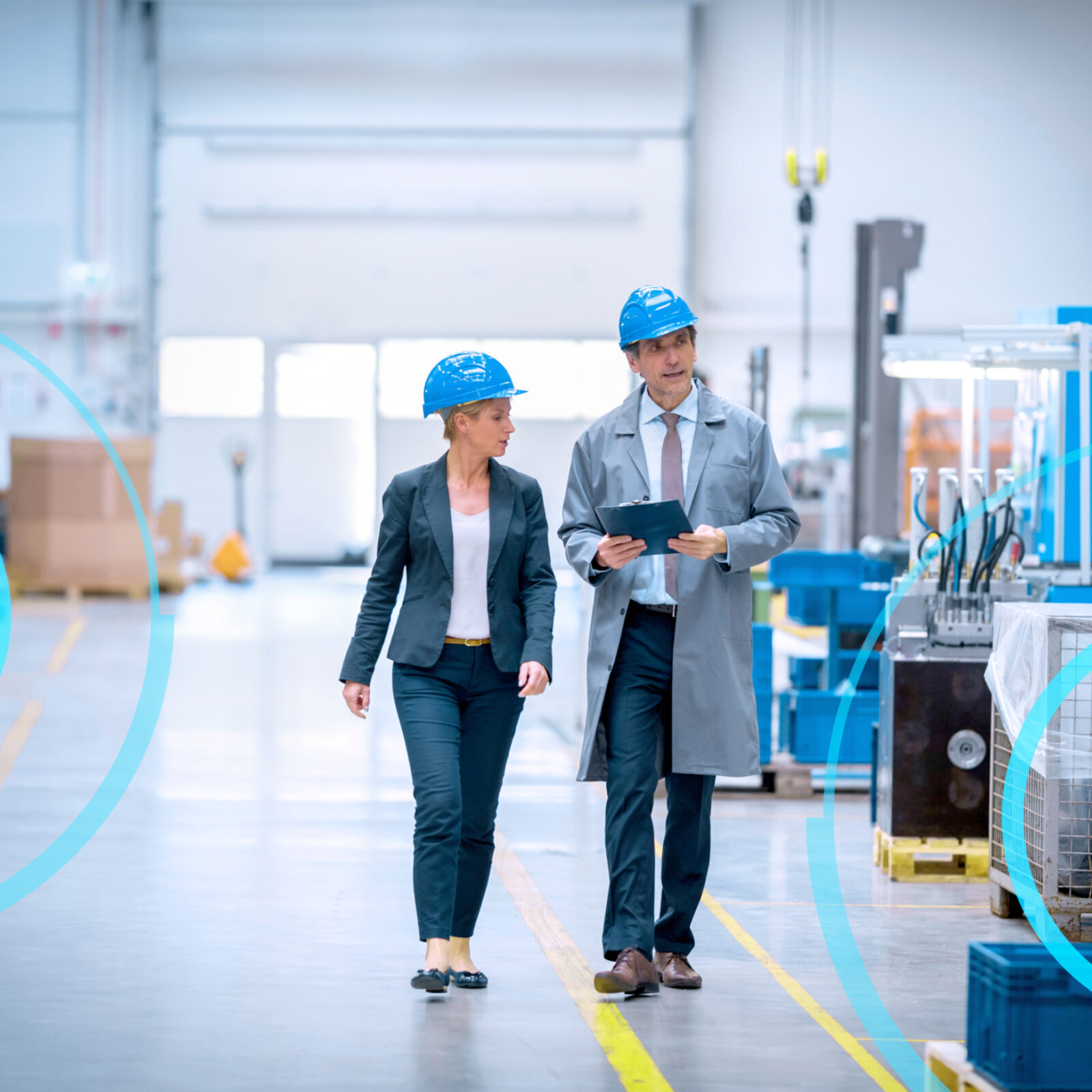 There are two people walking through a factory with a tablet an helmets on.