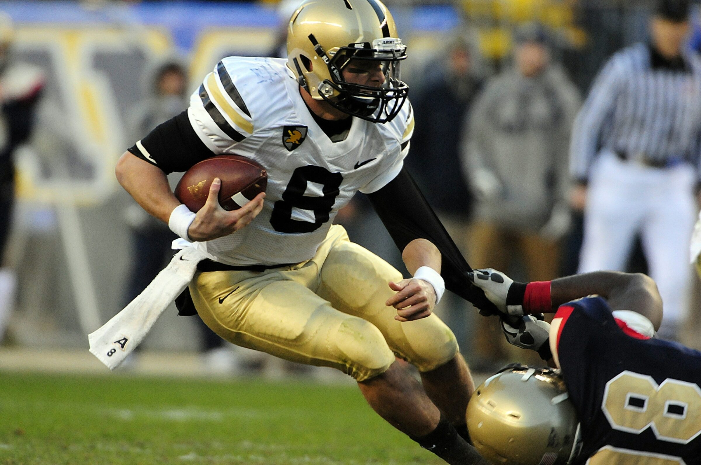 A football player makes a move to avoid a tackler during a game, while a player tracker monitors the athlete's performance and collects sports data.