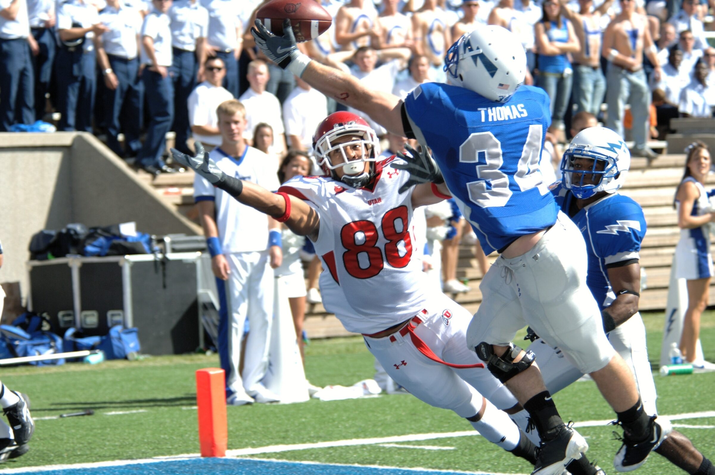 A wide receiver leaps to make a diving catch while a defender closes in on him, which puts them both at risk for a football injury.