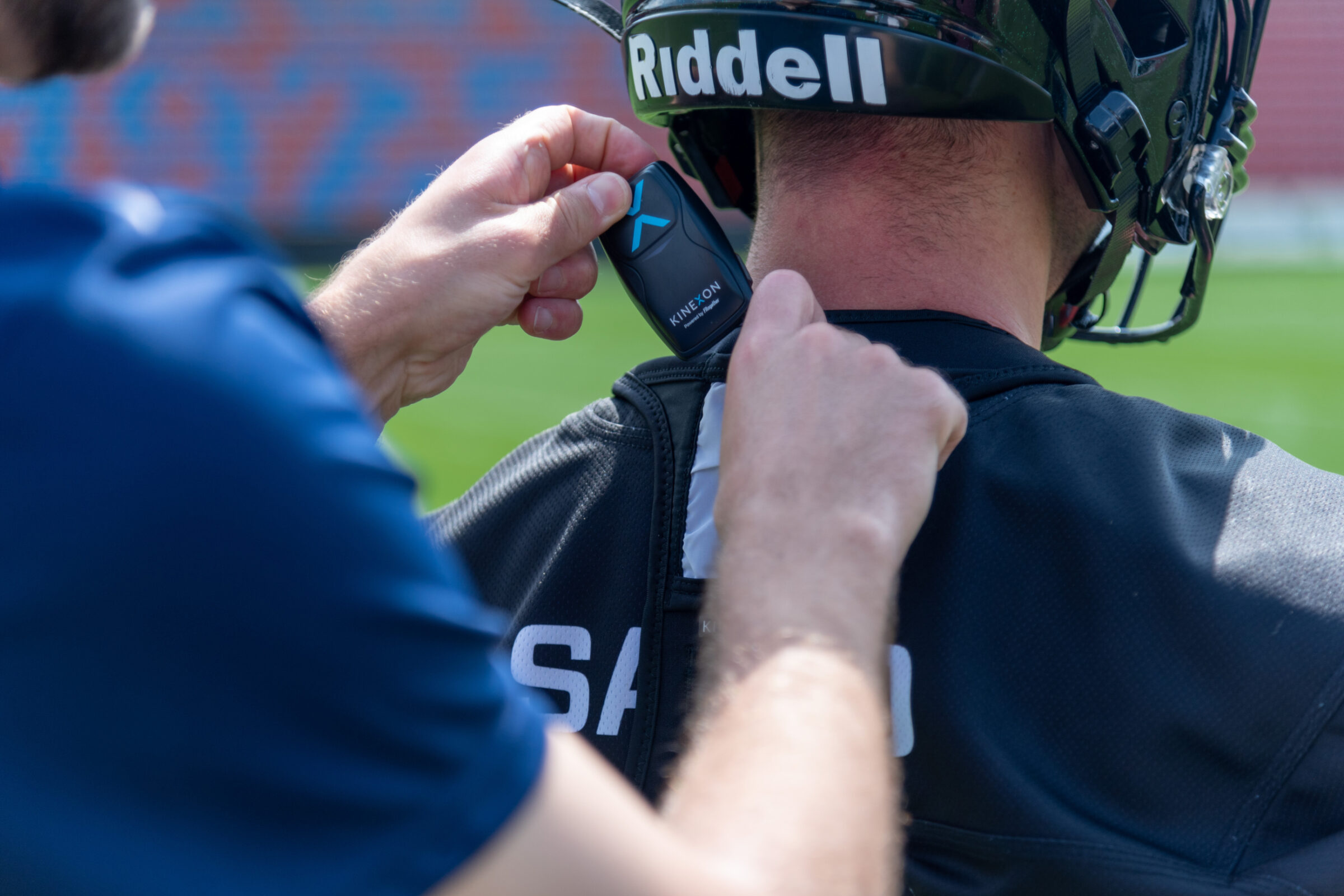 A tackle football player gets his gps athlete tracker from his coach, which slips into a lightweight vest and is not noticeable to the player.