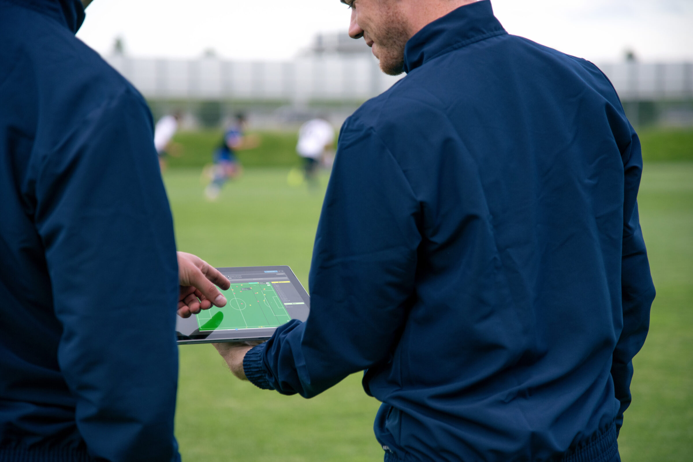 Two coaches analyze sports data they're getting from athlete trackers during a practice session.