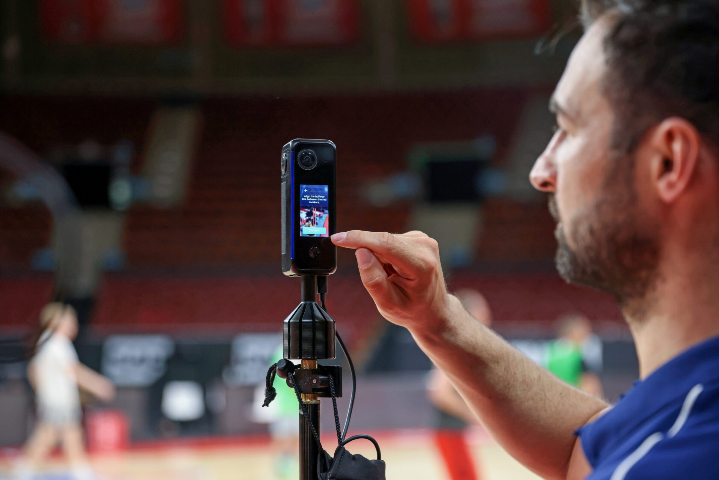 A coach sets up a video camera for basketball. The video will be uploaded to an app and analyzed by AI which provides analytics.