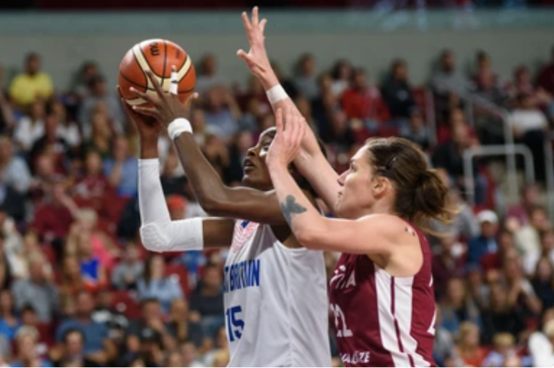 A women's basketball player in action, arm extended, releasing the ball towards the hoop.